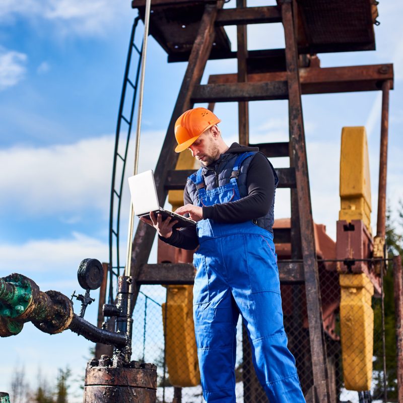 Petroleum engineer using laptop in oil field.