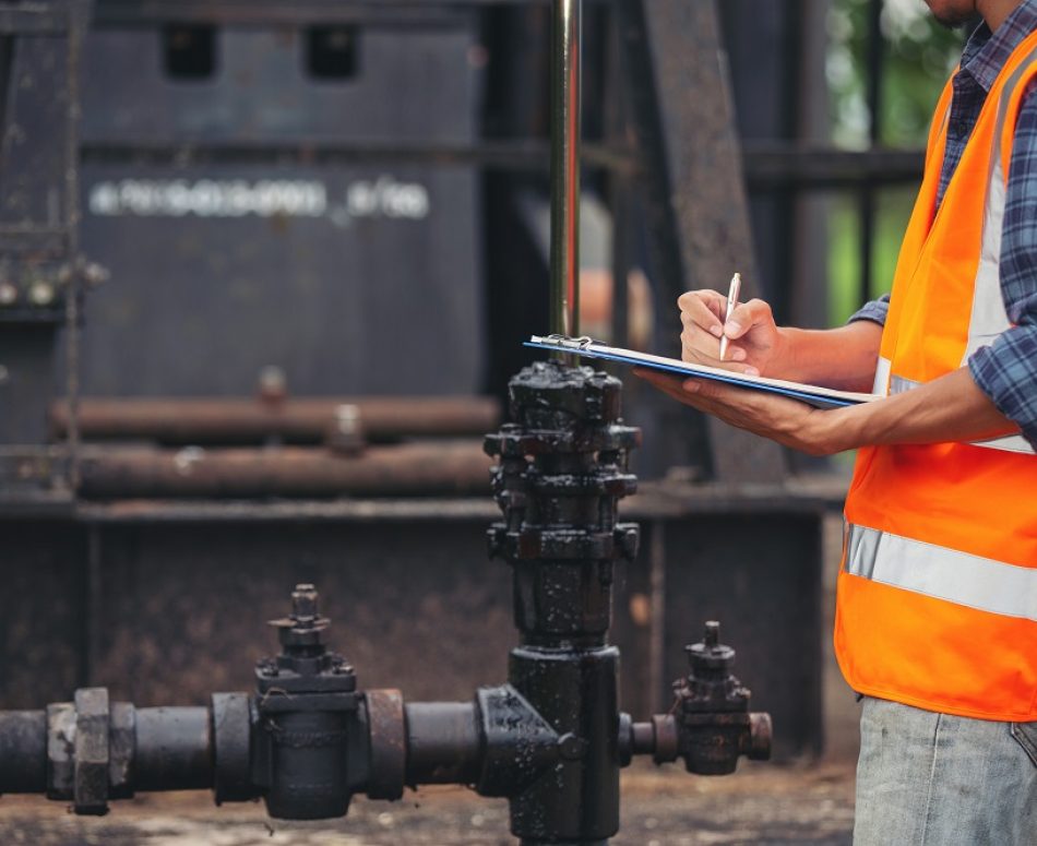Workers standing and checking beside working oil pumps.